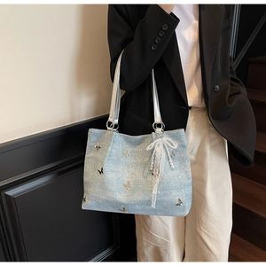 Detail of light blue denim tote bag with silver butterflies and pearl lace charm