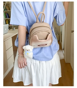 Detail view of cute cat face design and plush lamb charm on beige mini backpack