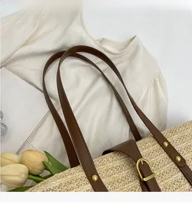 Close-up of woven straw tote bag featuring brown leather handles and gold metal buckles