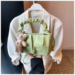 Detail of light green pleated leather shoulder bag with a brown plush bear charm