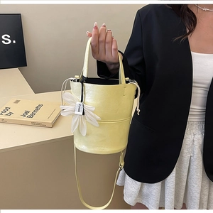 Detail of pale yellow leather bucket bag with white flower charm and adjustable strap