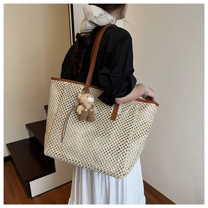 Détail d'un grand sac cabas en paille tissée avec anses en cuir brun et charm ours