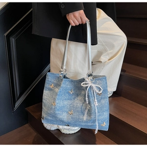 Detail of light blue denim tote bag with gold butterfly decals and a pearl lace bow