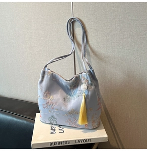 Detail of light blue embroidered bucket bag featuring floral patterns and yellow tassels