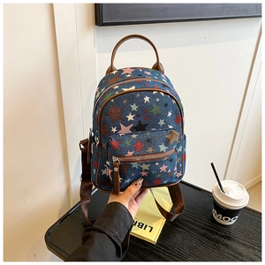 Close-up of mini denim backpack with star pattern held by hand in a cozy cafe setting