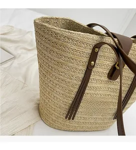 Close-up of woven straw tote bag featuring brown leather straps and metal rivets