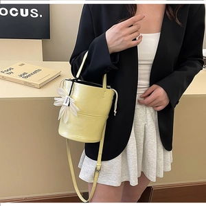 Detail view of yellow lychee grain leather bucket bag with a white daisy floral charm