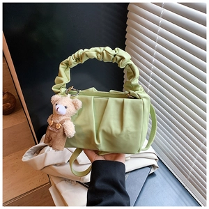Detail of light green pleated shoulder bag featuring a cute teddy bear charm and ruffles