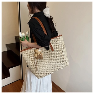 Détail d'un grand sac cabas en paille beige avec anses en cuir brun et un charm ours