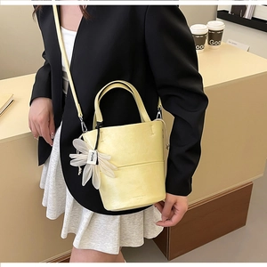 Close-up of cream yellow bucket bag with floral FUOR charm on a minimalist desk