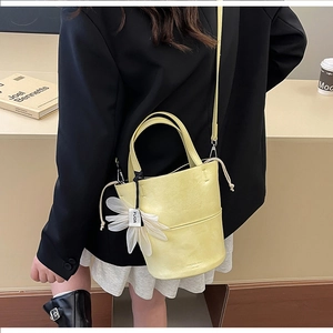 Detail of light yellow bucket bag featuring daisy charm and adjustable leather shoulder strap