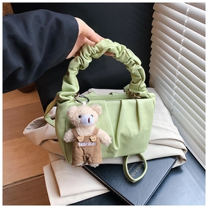 Detail of light green pleated underarm bag with a cute teddy bear charm on fabric