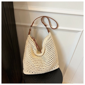 Detail of hollow-out beige straw shoulder bag with brown leather strap on wooden stool