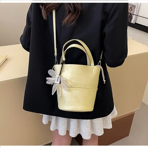 Detail of pale yellow bucket bag with smooth PU leather texture and floral charm