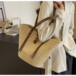 Detail of straw woven tote with brown leather strap and gold buckle on model