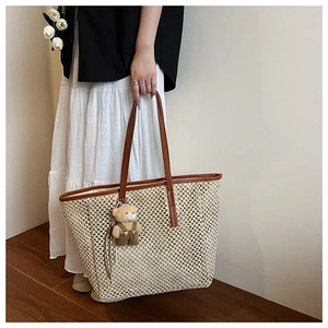 Détail du sac cabas en paille tissée avec poignées en cuir marron et pendentif ours mignon