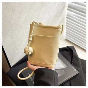 Close-up of light yellow litchi pattern mini crossbody bag with a decorative woven ball