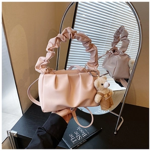 Detail of light pink pleated handbag with wide gathered handle and cute plush bear charm