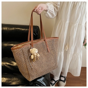 Détail d'un grand sac cabas en paille tressée avec un pendentif d'ours en peluche mignon