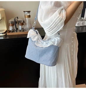 Detail of blue striped canvas shoulder bag featuring delicate white lace embroidery trim