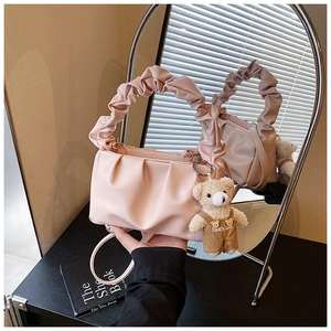 Detail of pink pleated handbag featuring a cute plush bear charm and matching strap
