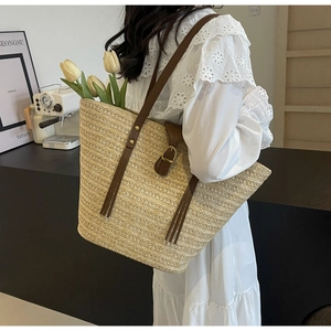 Close-up of straw woven tote bag with brown leather strap and gold hardware detail