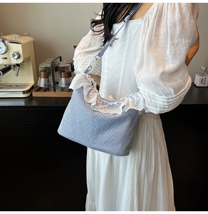 Blue and white striped canvas shoulder bag with delicate white lace trim on a model