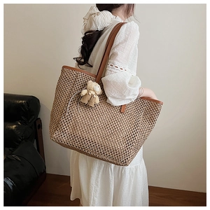 Détail d'un grand sac cabas en paille tissée avec poignées en cuir et breloque ours