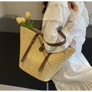 Close-up of woven straw tote bag with brown leather handles and yellow tulip accent