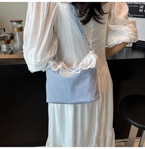 Detail of blue striped tote bag featuring white lace trim and metal strap hooks
