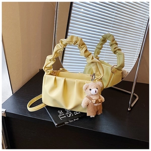 Detail of yellow pleated shoulder bag with a cute teddy bear charm on black furniture