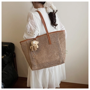 Détail d'un grand sac cabas en paille avec bordure en cuir marron et breloque ours mignon