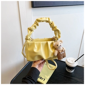 Detail showing bright yellow pleated shoulder bag with teddy bear charm and strap