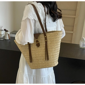 Detail of hand-woven straw tote bag with brown leather straps and metallic buckle accent
