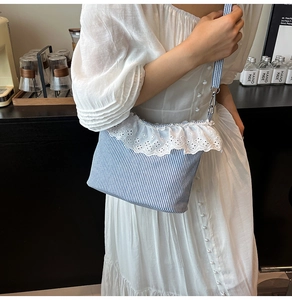 Detail of blue striped canvas bag with lace trim worn with a white puff sleeve dress