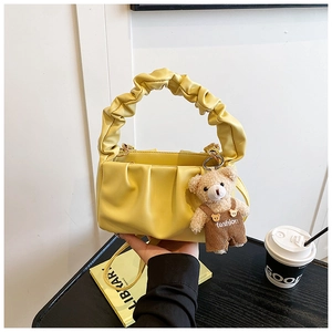 Detail of yellow pleated shoulder bag with a cute bear pendant and a slim strap