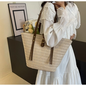 Detail of cream straw tote bag with brown leather handles worn by model in a chic setting