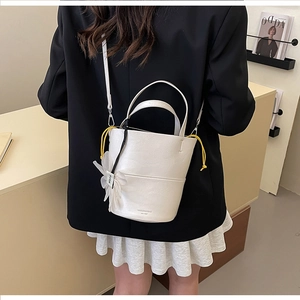 Detail view of a white leather bucket bag with daisy charm and yellow drawstring closure
