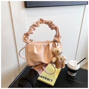 Detail of light pink pleated handbag with a cute brown bear charm and long shoulder strap