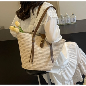 Woven straw tote bag detail with brown leather straps and stylish decorative tassels