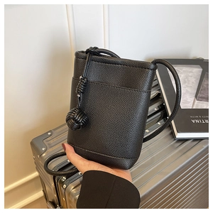 Close-up of black litchi grain leather mini crossbody bag with woven ball charm detail