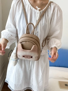 Cute cartoon cat beige mini backpack with plush pendant worn by a model in a bedroom