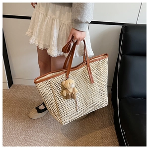 Détail d'un sac cabas en paille beige avec des anses en cuir marron et un charme d'ourson