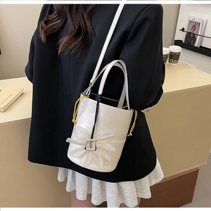 Detail of white leather bucket bag featuring a large floral charm and yellow drawstring