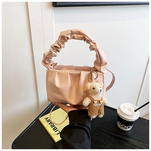 Detail of pink pleated handbag with cute bear charm on a minimalist desk setting
