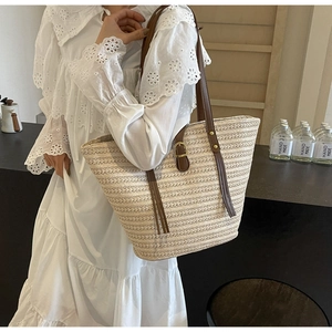 Detail of woven straw tote bag with brown leather straps and metal buckle closure