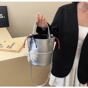 Detail of silver metallic bucket bag featuring pleated texture and red drawstring with flower