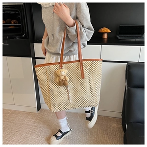 Détail d'un grand sac en paille tressée avec anses en cuir marron et pendentif ours
