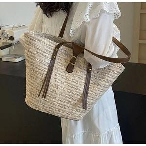 Close-up of woven straw tote bag with brown leather straps and gold buckle detail