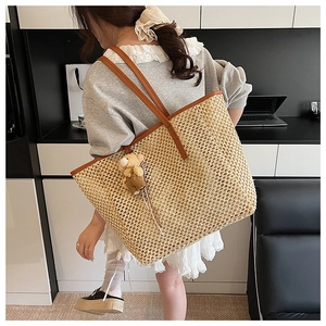 Détail d'un grand sac fourre-tout en paille avec lanières en cuir brun et breloque